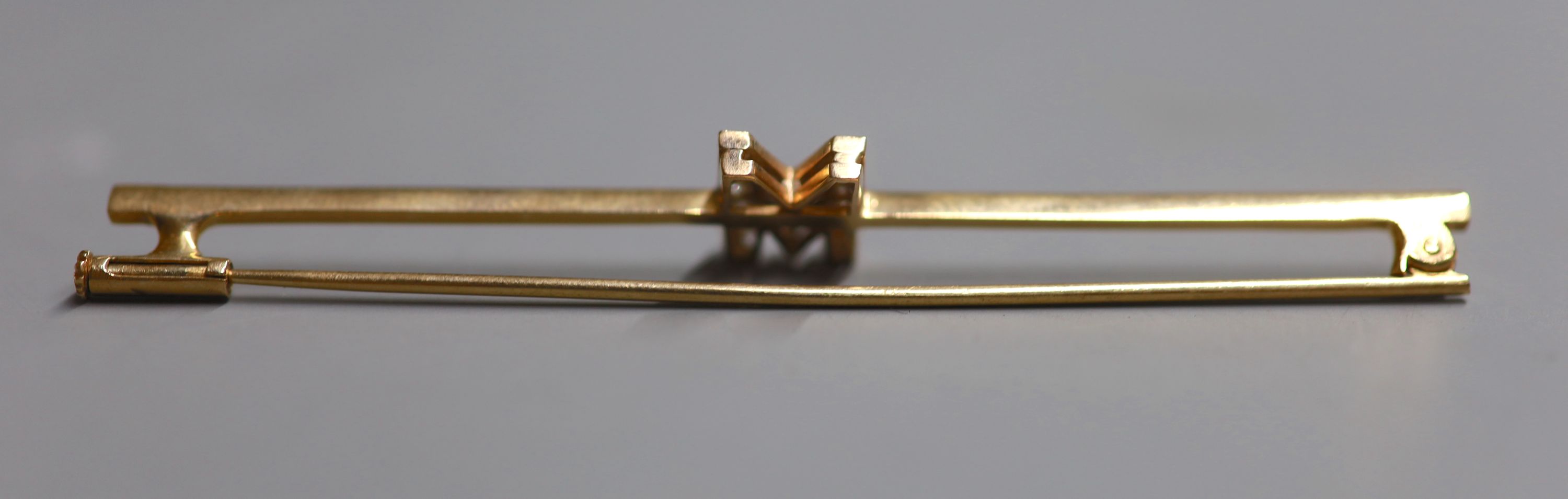 A yellow metal and diamond set initial M bar brooch, 77mm, gross 4.6 grams.